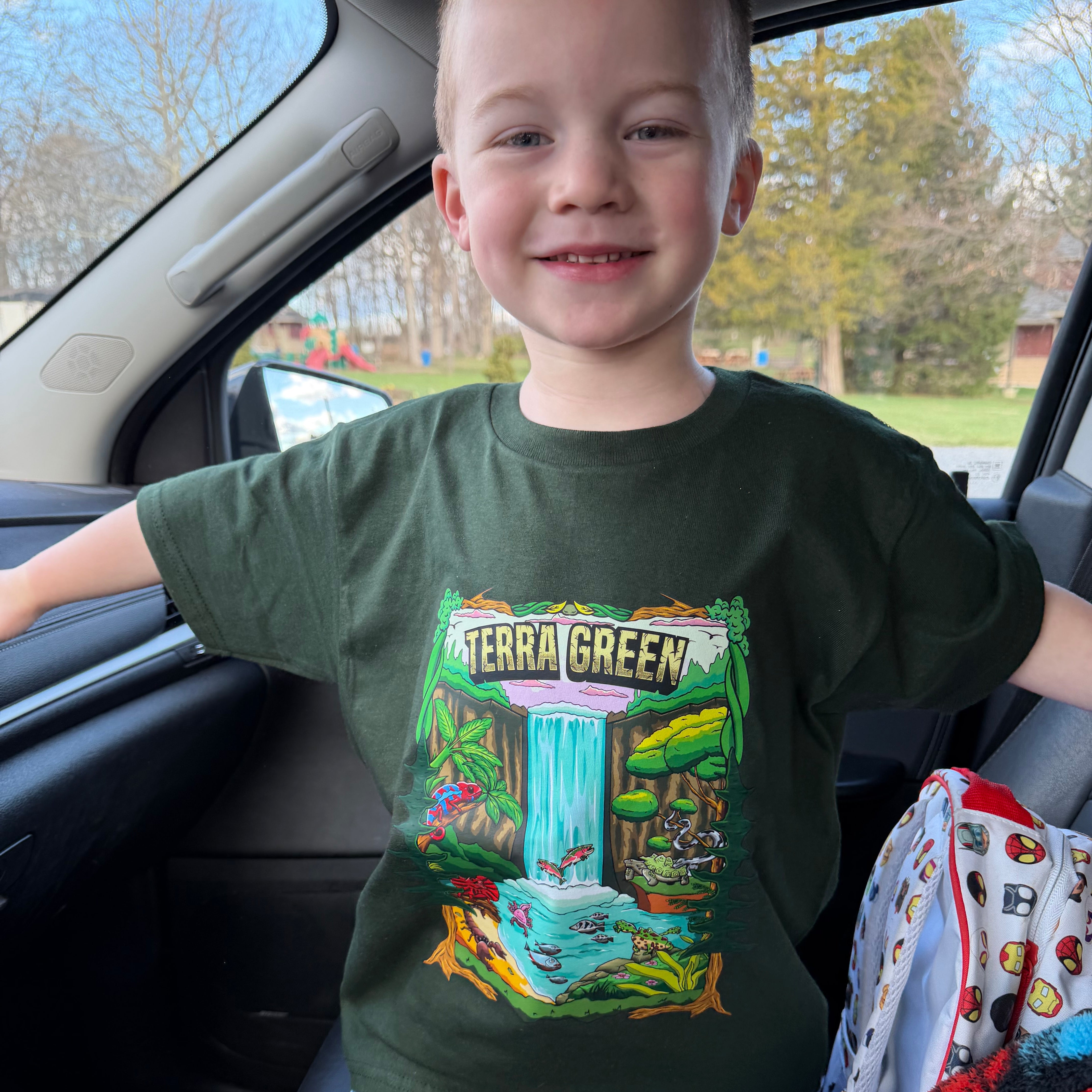 Child wearing a green t-shirt with a colorful graphic design inside a vehicle.